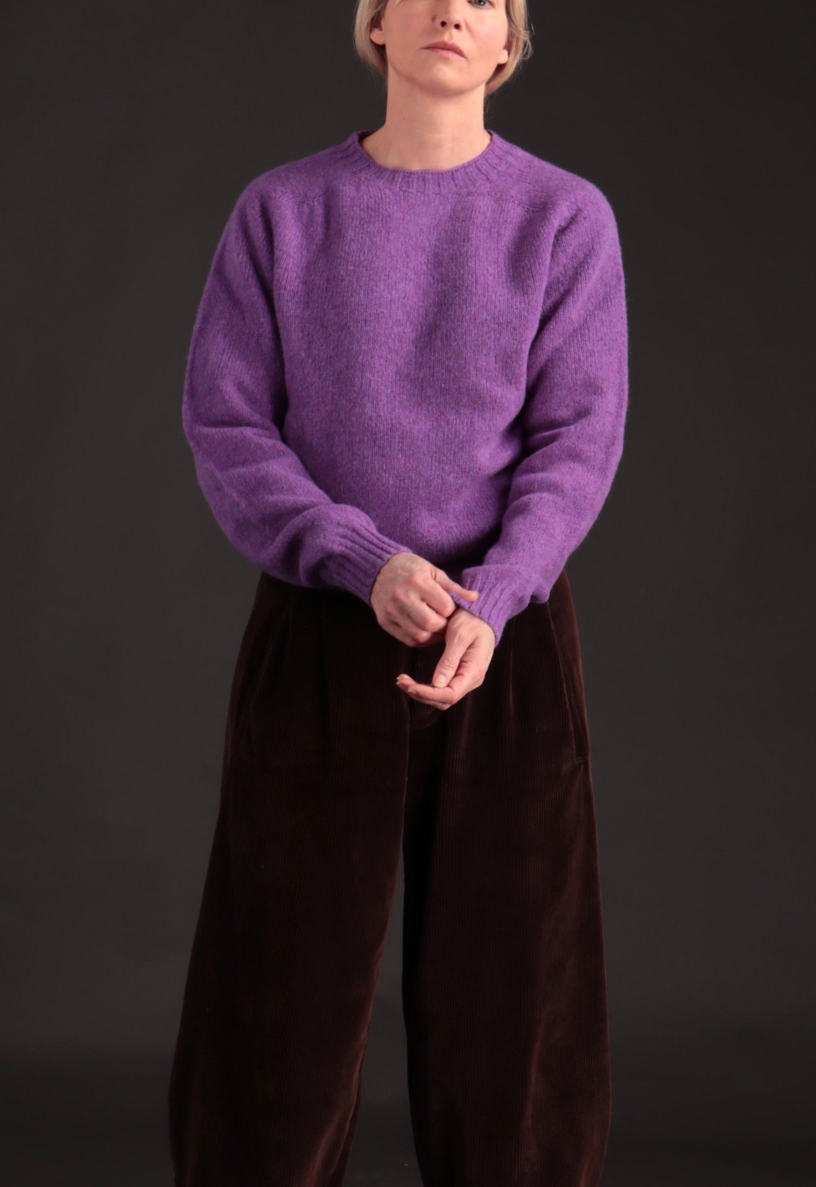 Woman wears Carrier Company Shetland Lambswool Jumper in Allium with Dutch Trouser in Chocolate Corduroy