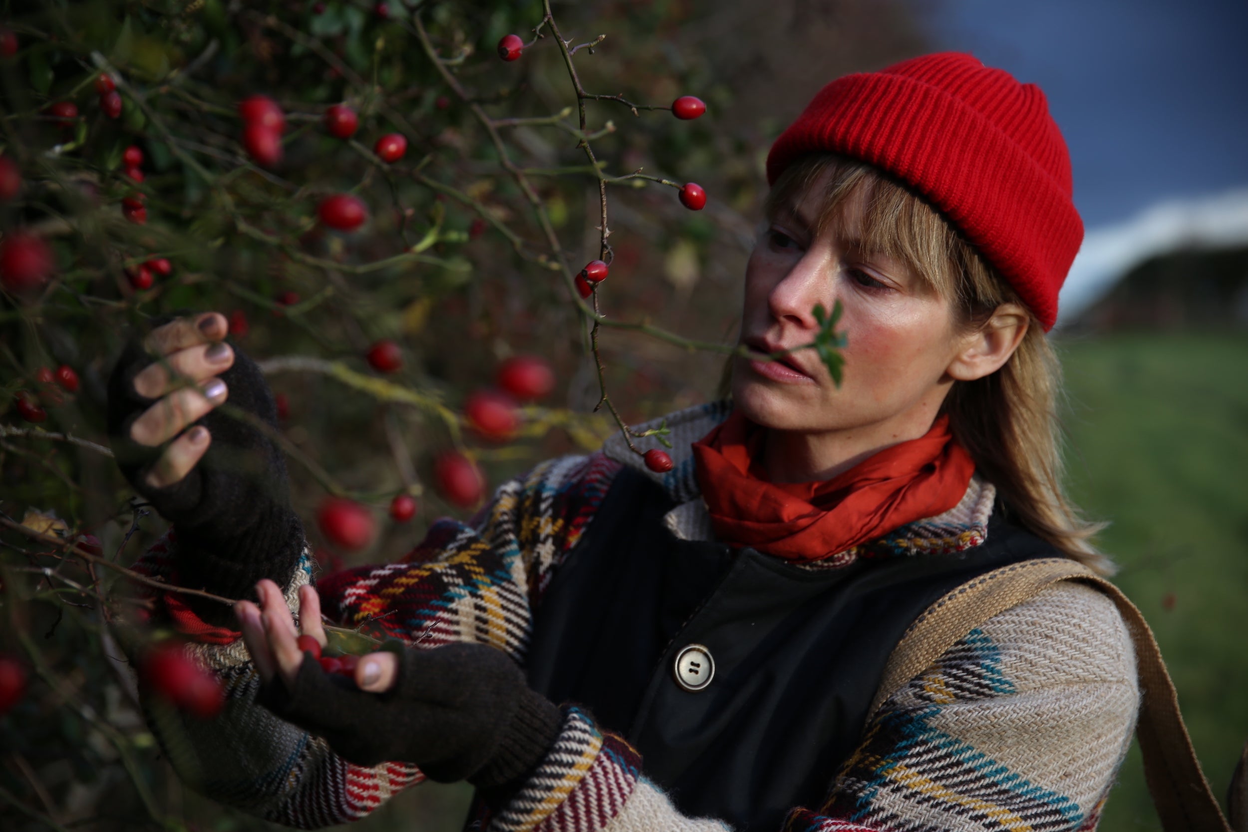 Woman wears Carrier Company Wool Hat in Poppy Red with Celtic Wool Jacket and Gathering Glove