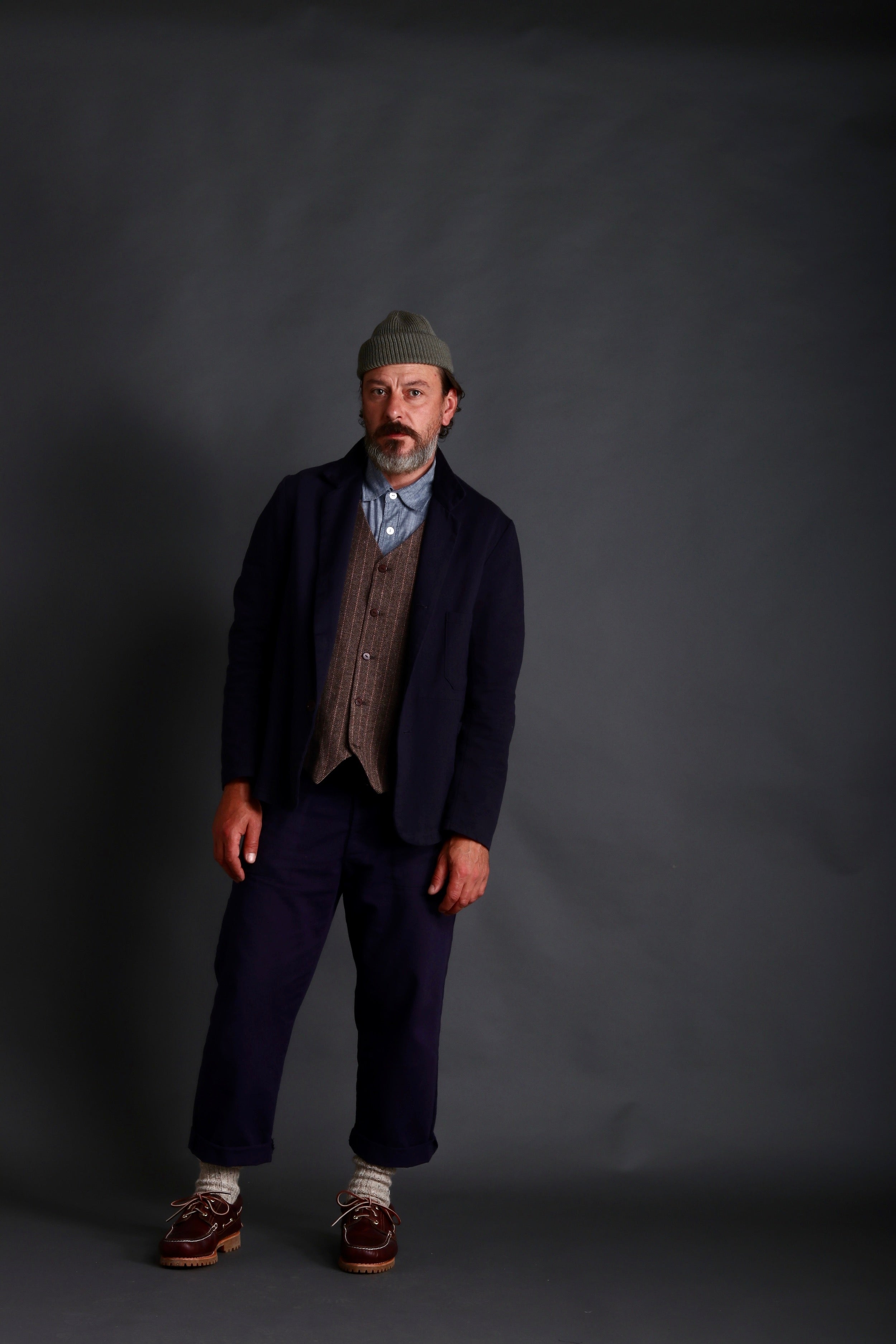 Man wears Carrier Company 3 Button Jacket in Navy Drill with Classic Trouser, Chambray Shirt and Wool Waistcoat