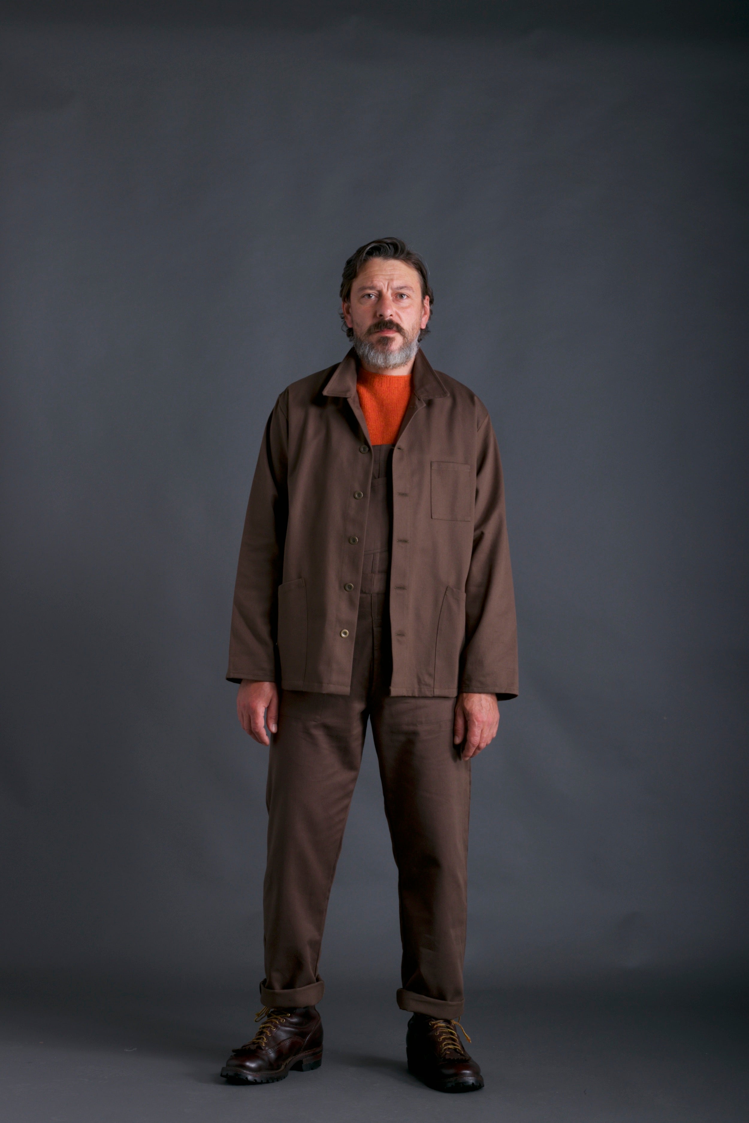 Man wears Traditional Work Jacket in Olive with Olive Dungarees and Tangerine Lambswool Jumper