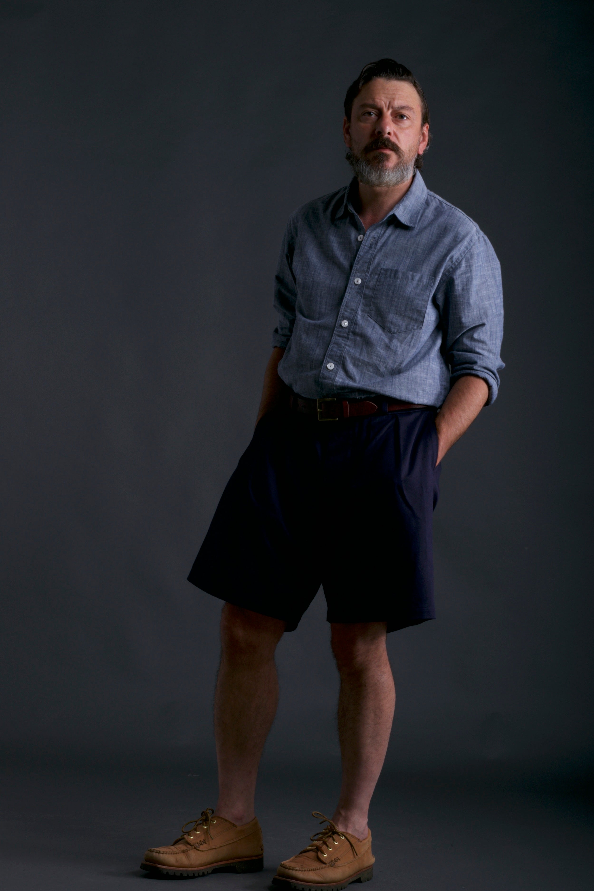 Man wears Carrier Company Grandpa Shorts in Navy with Chambray Shirt