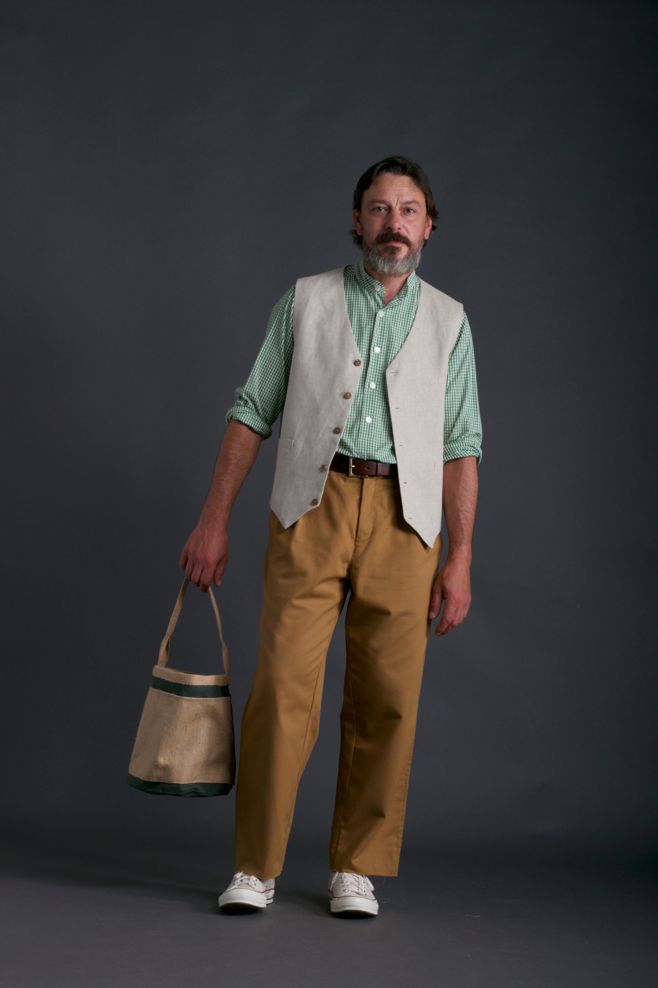 Man wears Carrier Company Men's Linen Waistcoat with Collarless Shirt in Green Gingham and Classic Trouser in Tan