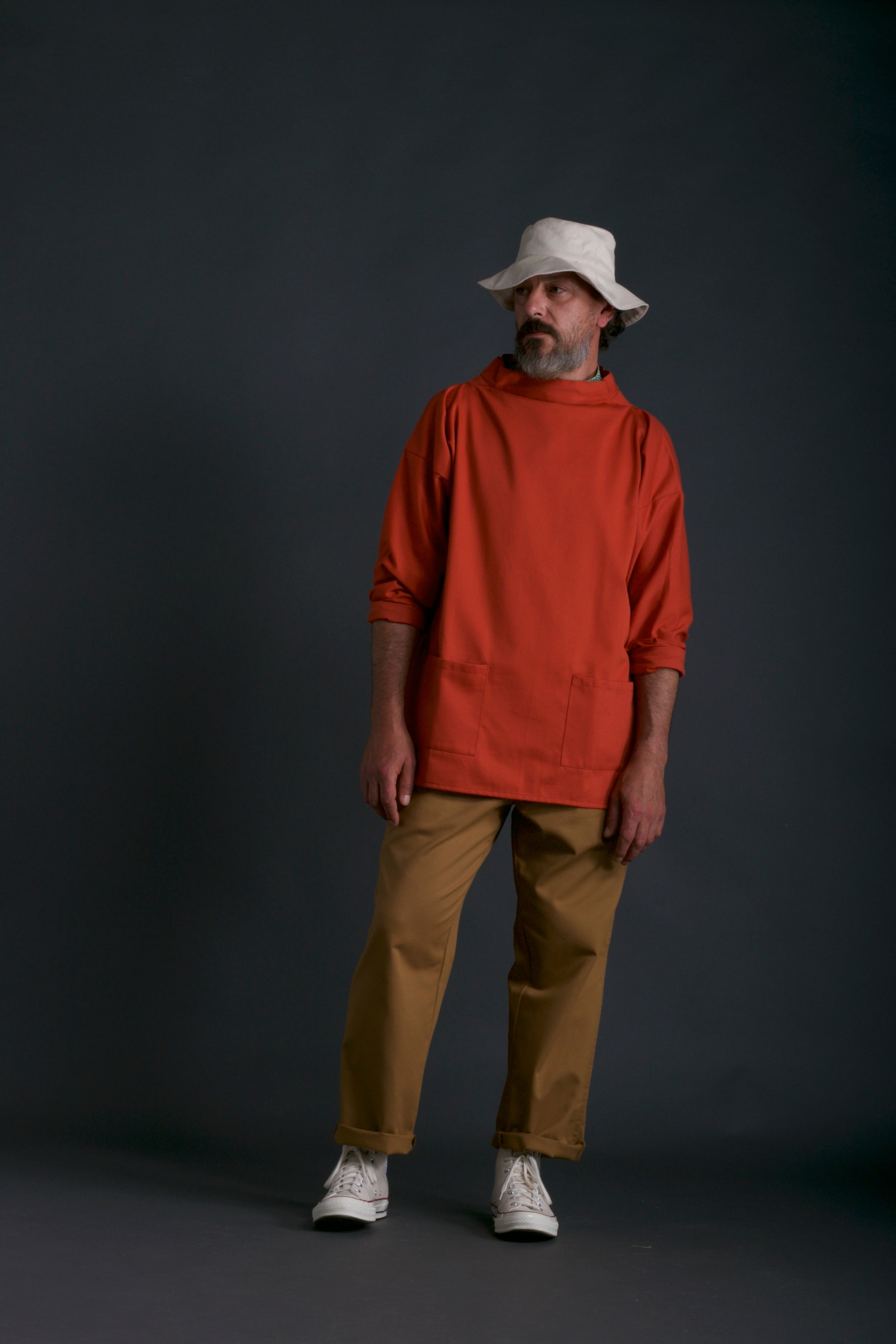 Man wears Carrier Company Traditional Norfolk Slop in Orange with Classic Trouser in Tan and Sun Hat