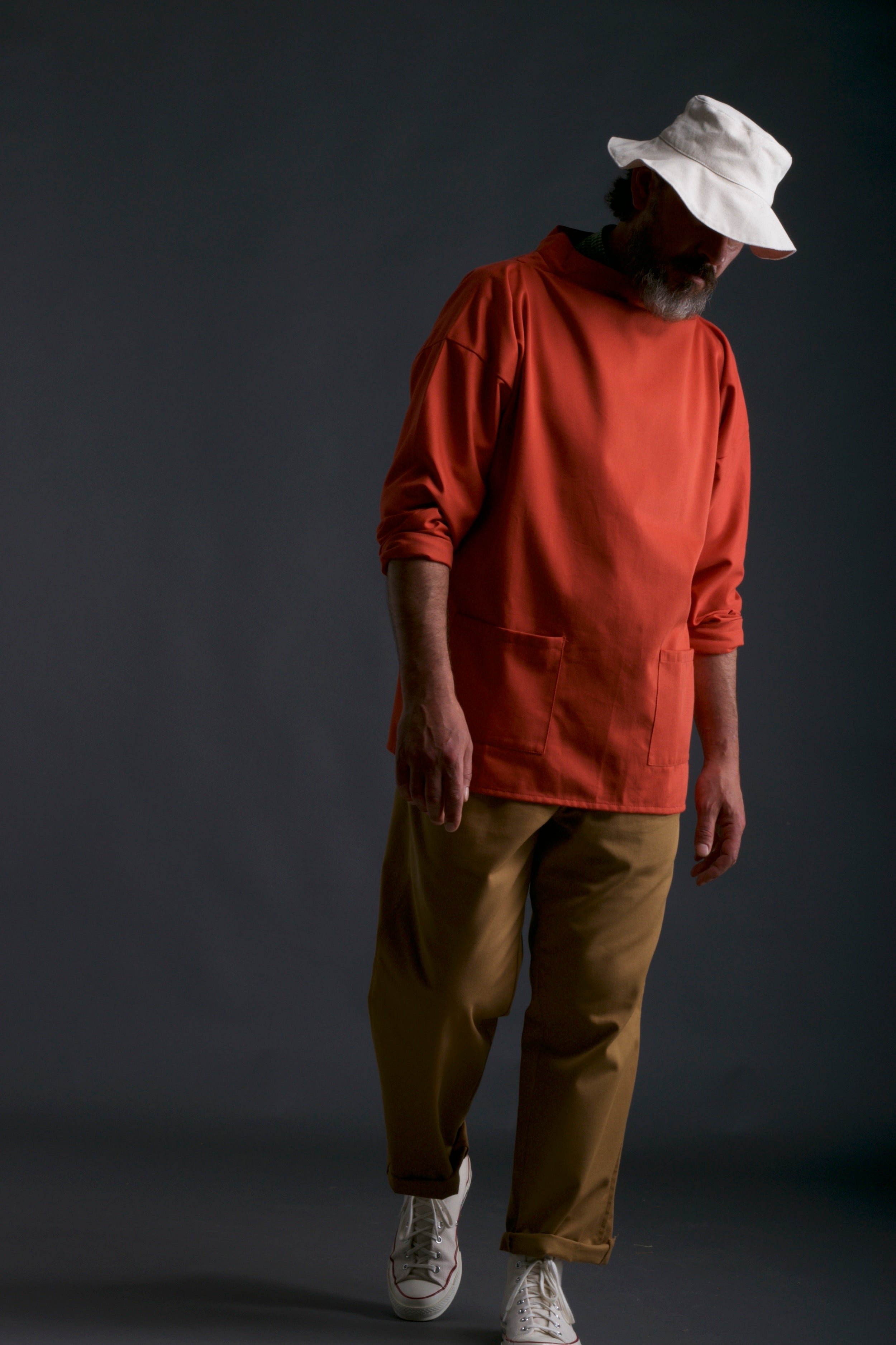 Man wears Carrier Company Traditional Norfolk Slop in Orange with Classic Trouser in Tan and Sun Hat