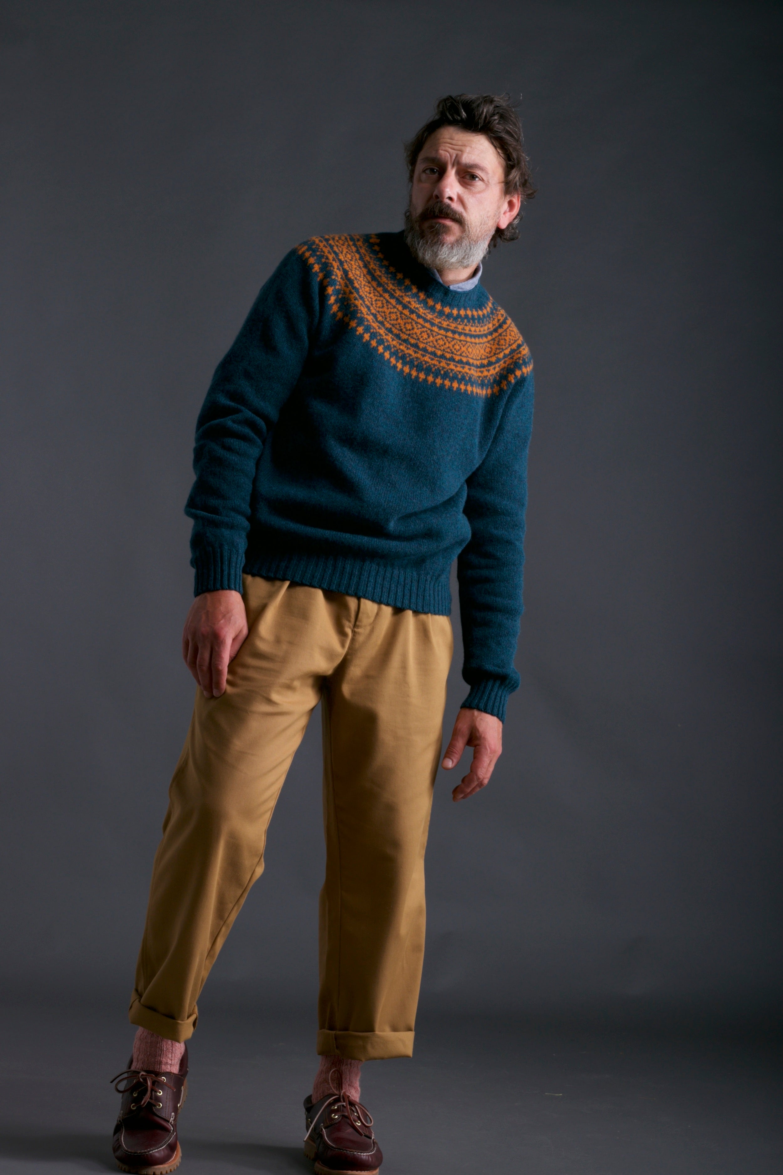 Man wears Carrier Company Shetland Yoke Jumper in ginger and Teal with Mens Work Trouser in Tan