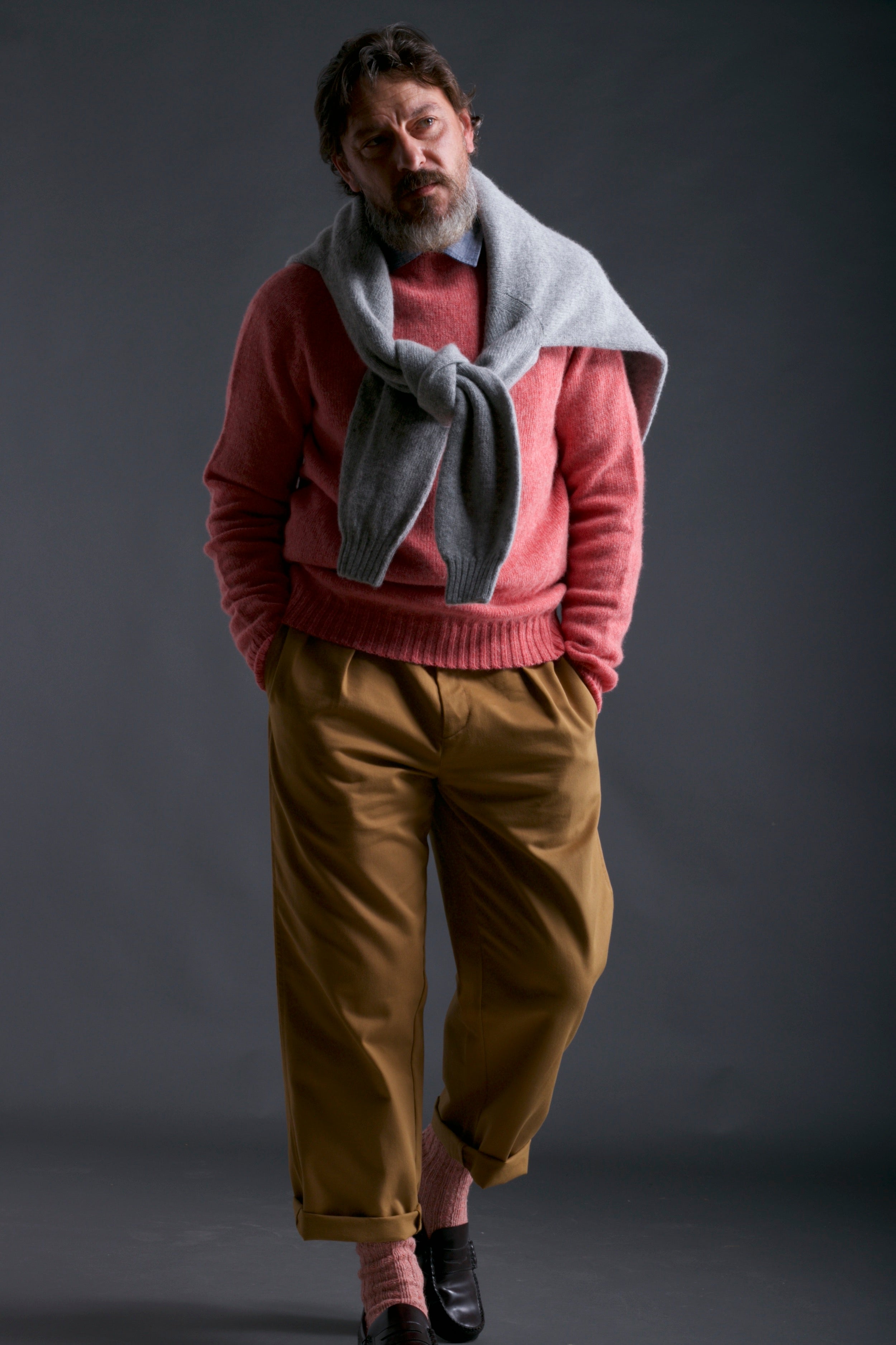 Man wears Carrier Company Shetland Lambswool Jumper in Salmon with Chambray Shirt and Classic Trouser in Tan