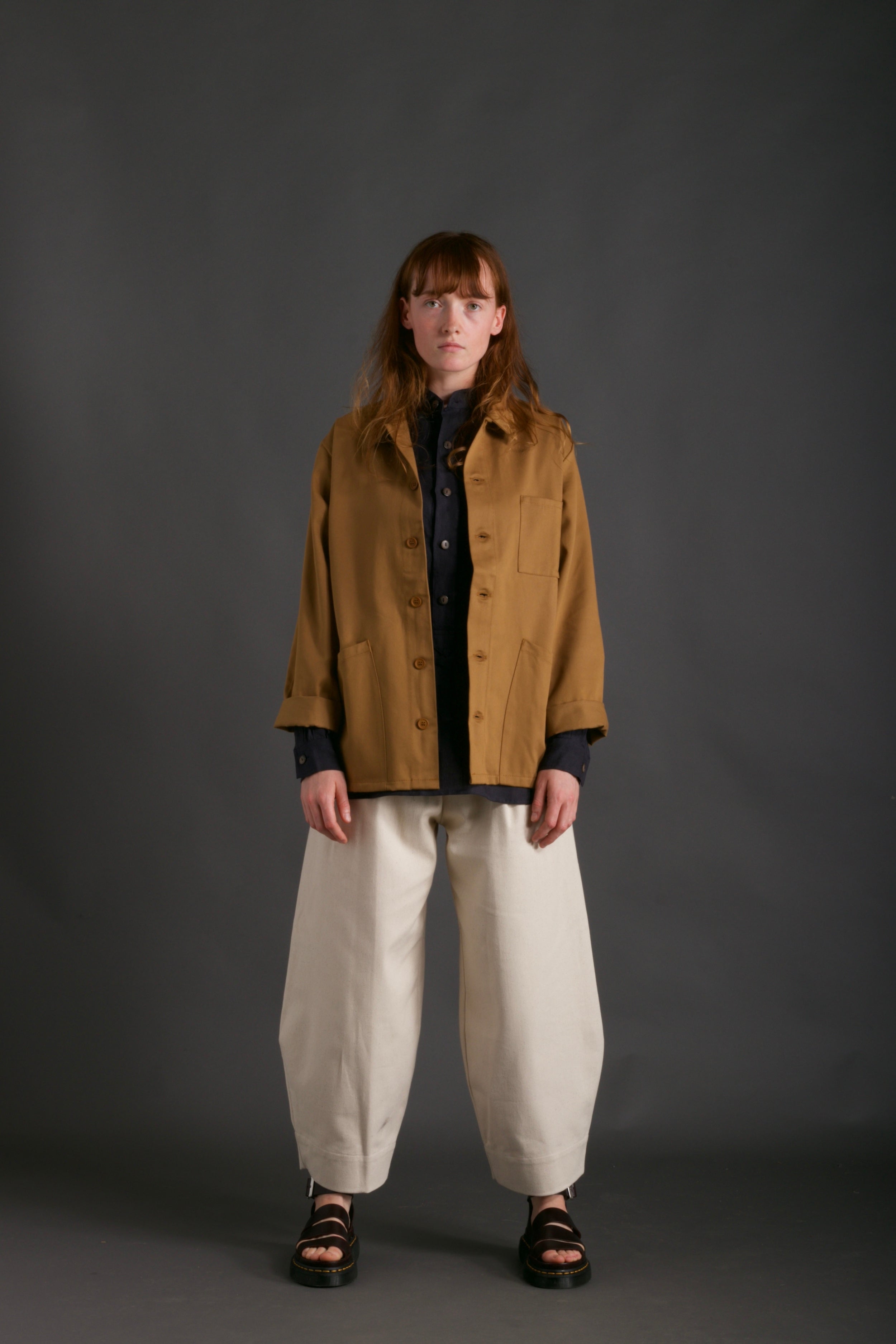 Woman wears Carrier Company Work Jacket in Tan with Dutch Trouser in Seeded Denim and Collarless Work Shirt in Navy Linen