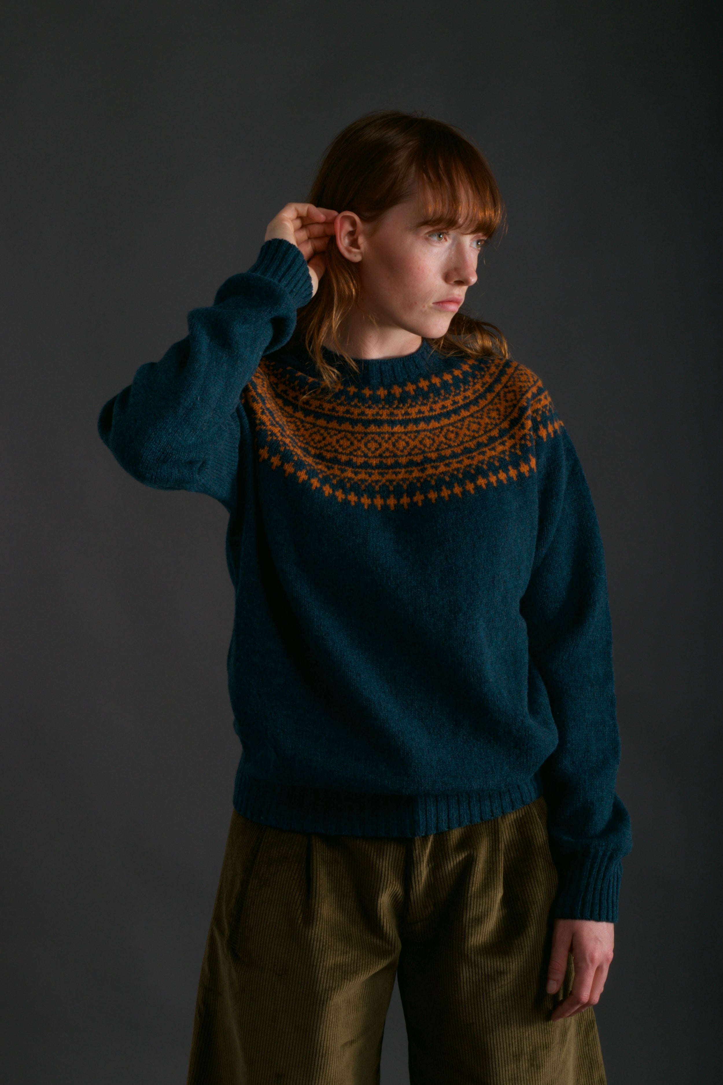 Woman wears Carrier Company Shetland Yoke Jumper in ginger and Teal with Dutch Trouser in Corduroy