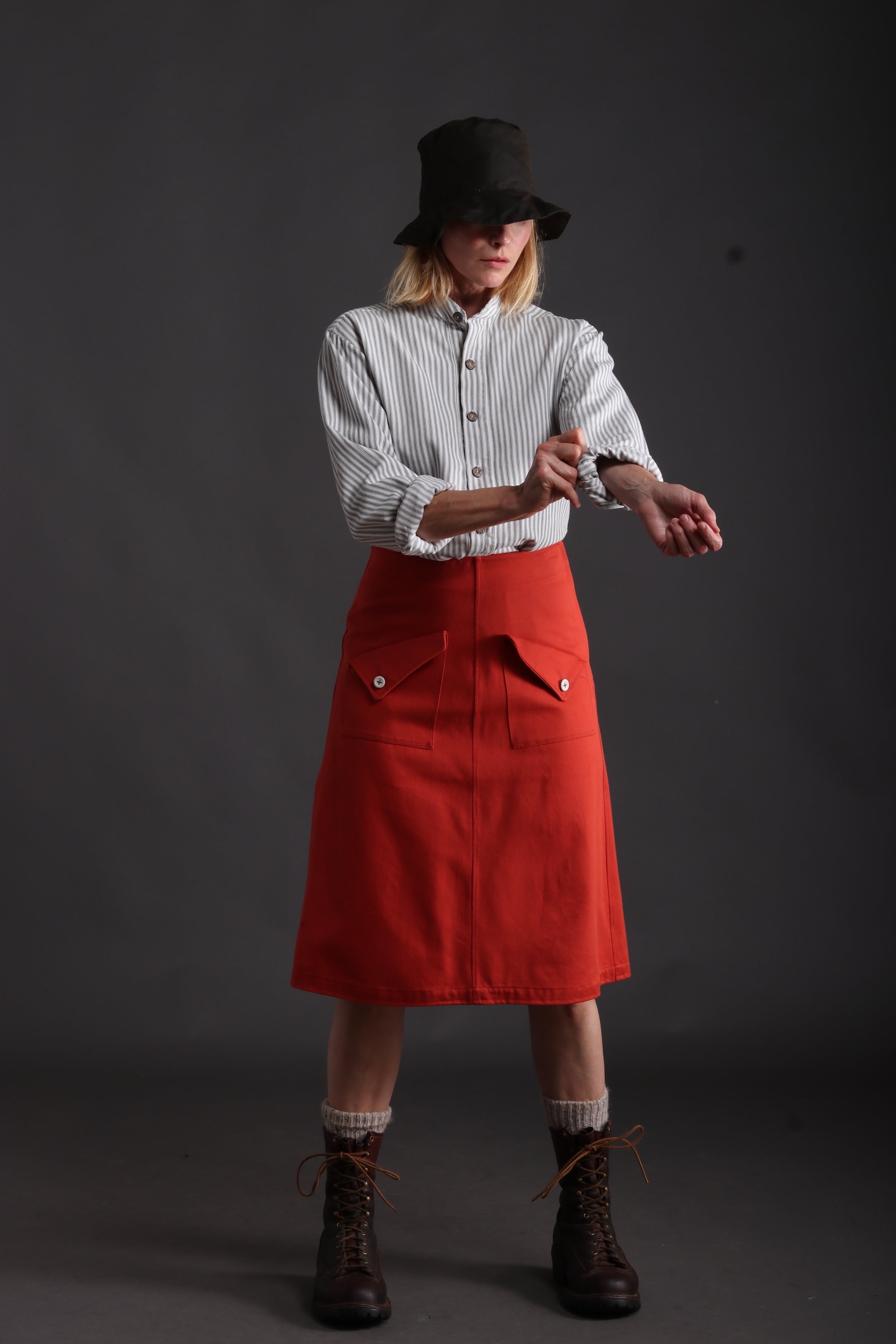 Woman wears Carrier Company Mum Skirt in Orange with Collarless Ticking Work Shirt and Rain Hat