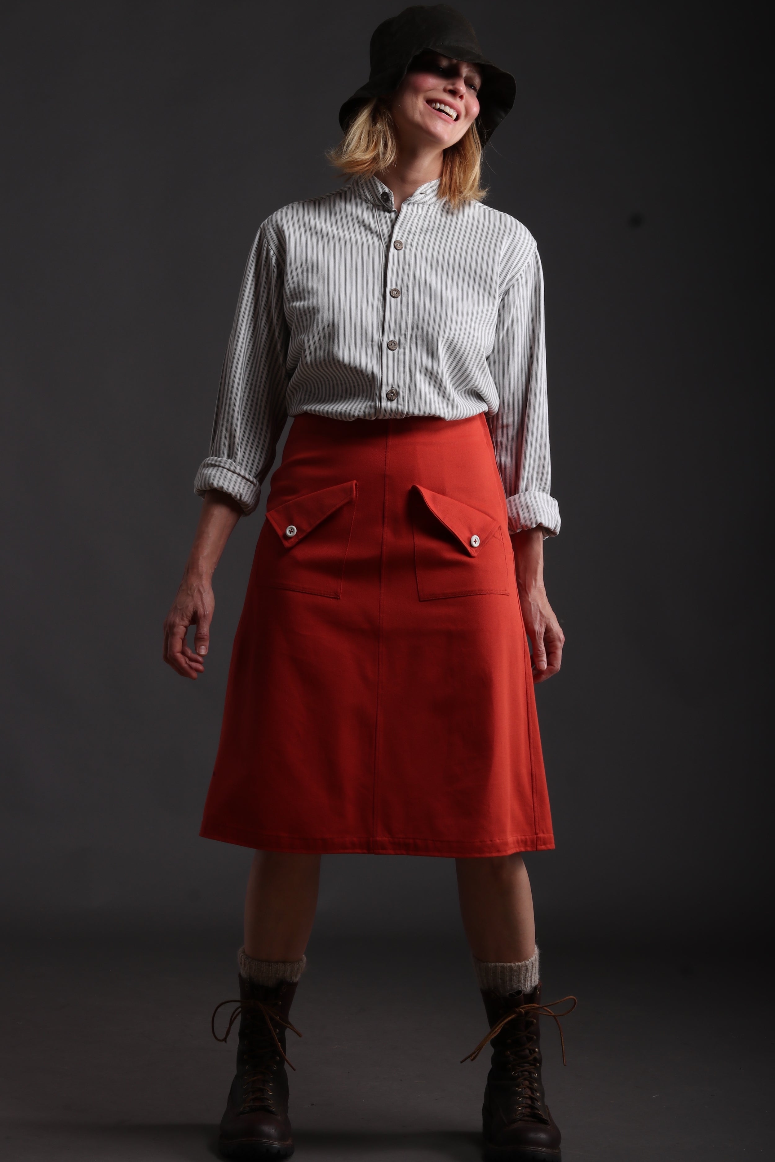 Woman wears Carrier Company Mum Skirt in Orange with Collarless Ticking Work Shirt and Rain Hat