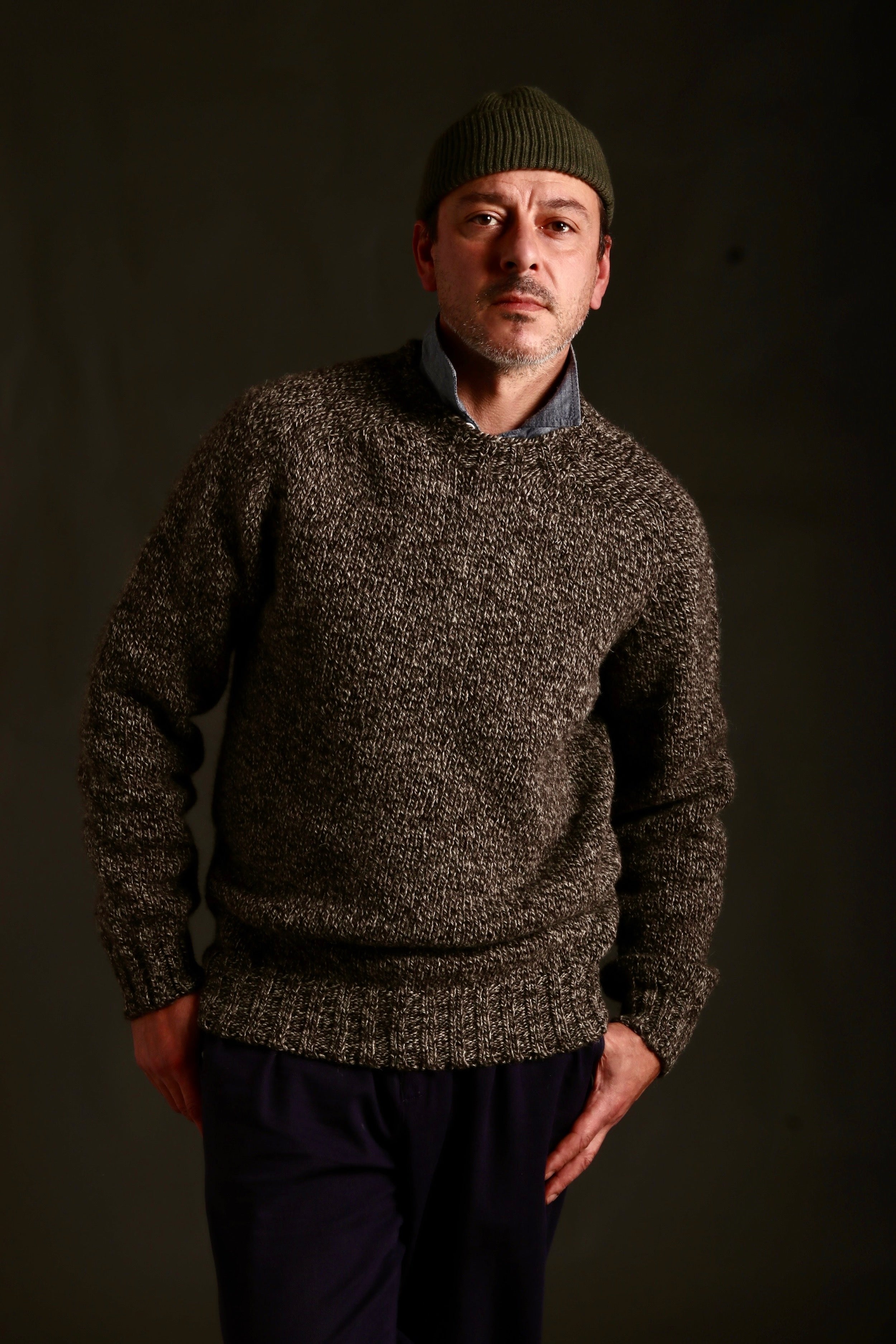 Man wears Carrier Company Heavy Heritage Wool jumper in Jacob, a blend of natural undyed wool ranging from Cream to Tan to Brown to Black, woven together to create an overall dark speckled appearance, Worn with Mens Classic Trouser and Wool Hat in Olive Drab