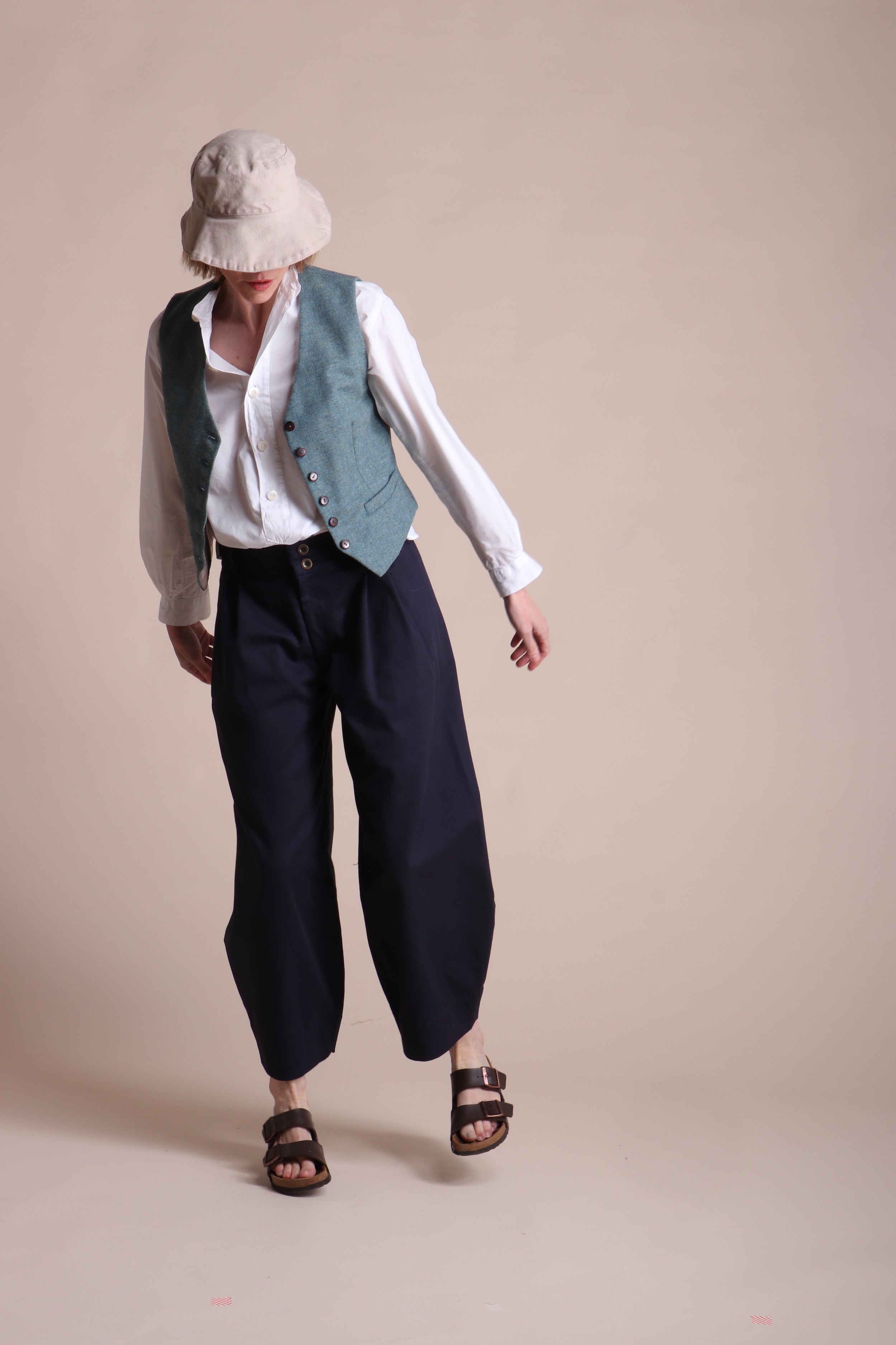 Woman wears Carrier Company Lightweight Collarless Shirt with Dutch Trouser In Navy Drill, Women's Wool Waistcoat in Marine and Cotton Sun Hat