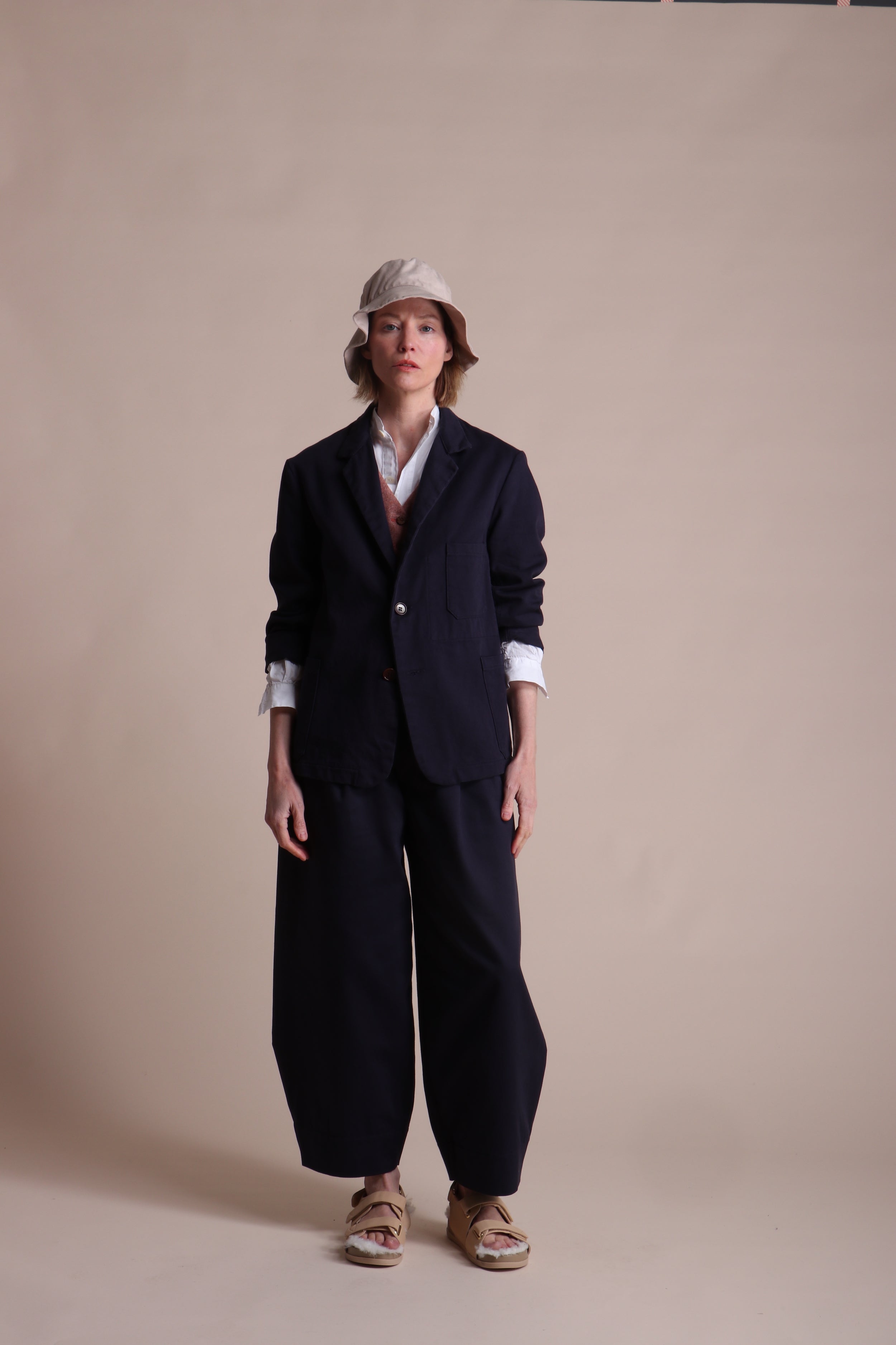 Woman wears Carrier Company 3 Button Jacket in Navy Drill with Dutch Trouser in Cotton, Lightweight Collarless Shirt and Wool Waistcoat in Coral