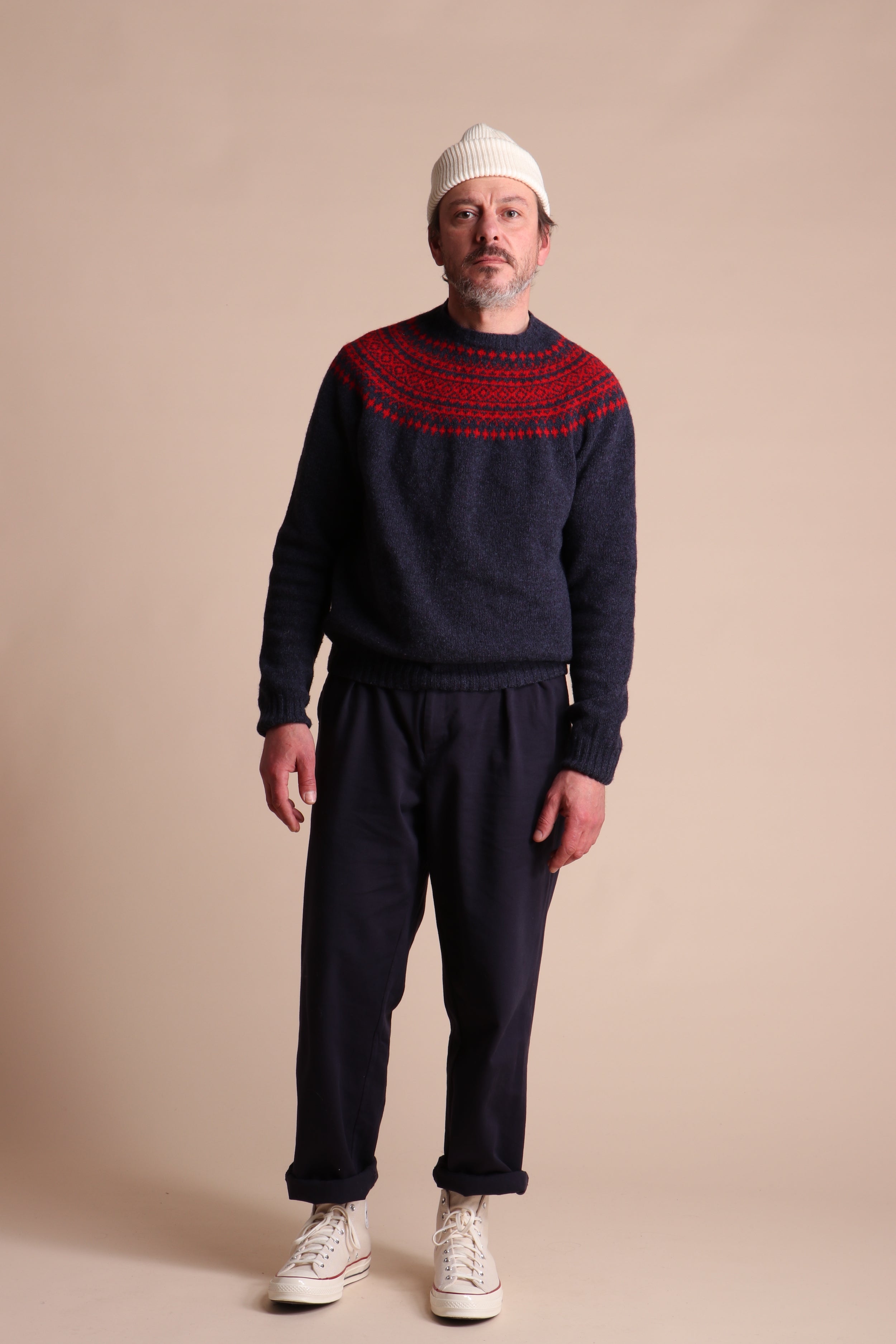 Man wears Carrier Company Shetland Lambswool Yoke Jumper in Ruby & Navy with Classic Trouser and Wool hat