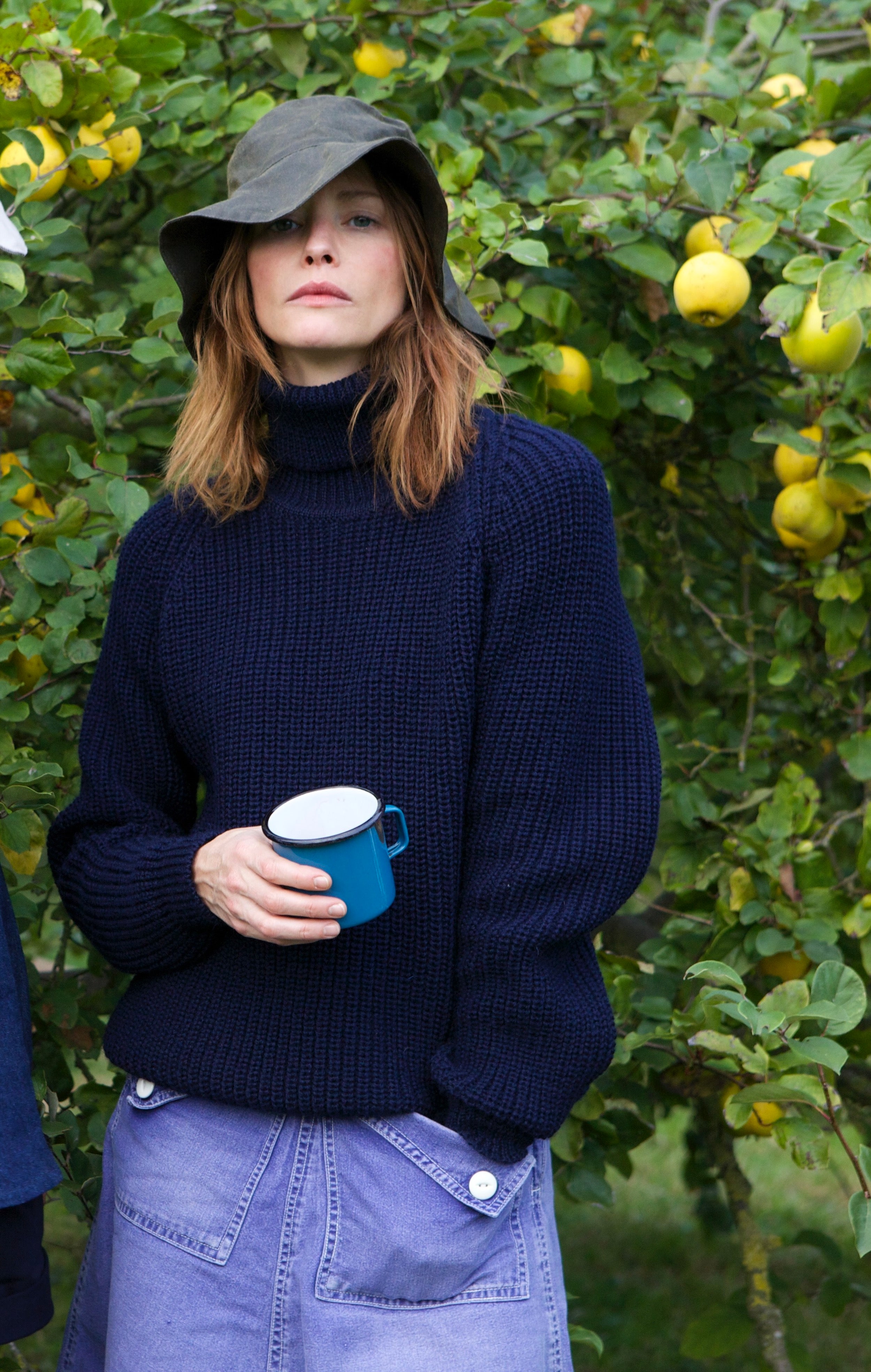 Woman wears Carrier Company Waxed Cotton Hat in Olive with Fisherman's Jumper and Mum Skirt