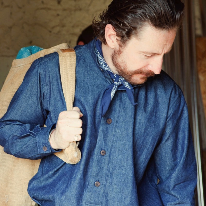 Man wearing the Carrier Company Demin Work Shirt with blue neckerchief and carrying a beige canvas bag