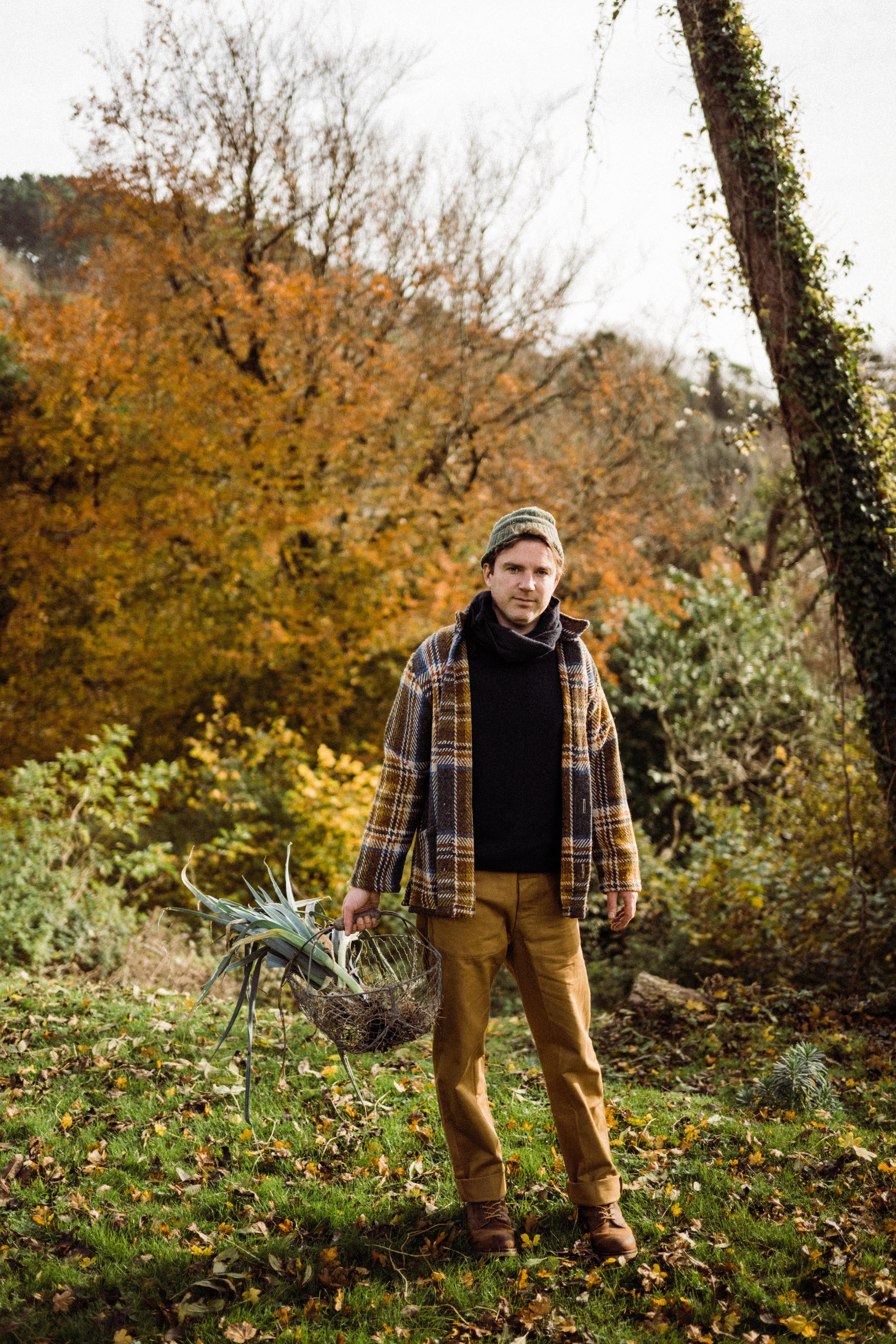 Man wears Carrier Company Celtic Wool Jacket in Slate & Russet with Traditional Guernsey and Men's Work Trouser in Tan